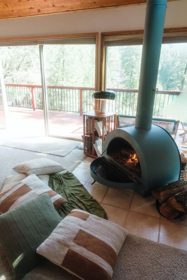 A cozy living room with a wood-burning stove, a comfortable sofa, and a view of the outdoors. - Private Lakefront Sanctuary | Cedar Hot Tub + 6 Acres, No Neighbors (Nevada City)