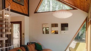 A modern living room with a wooden ceiling, a curved sofa, a green stool, and a yellow chair. - Private Lakefront Sanctuary | Cedar Hot Tub + 6 Acres, No Neighbors (Nevada City)