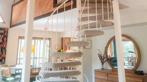 A spacious living area with a spiral staircase, wooden beams, and a dining area with chairs and a table. - Private Lakefront Sanctuary | Cedar Hot Tub + 6 Acres, No Neighbors (Nevada City)