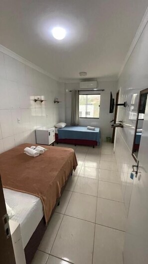 Une chambre d’hôtel avec deux lits, une petite table, un appareil de climatisation et une fenêtre avec des rideaux.