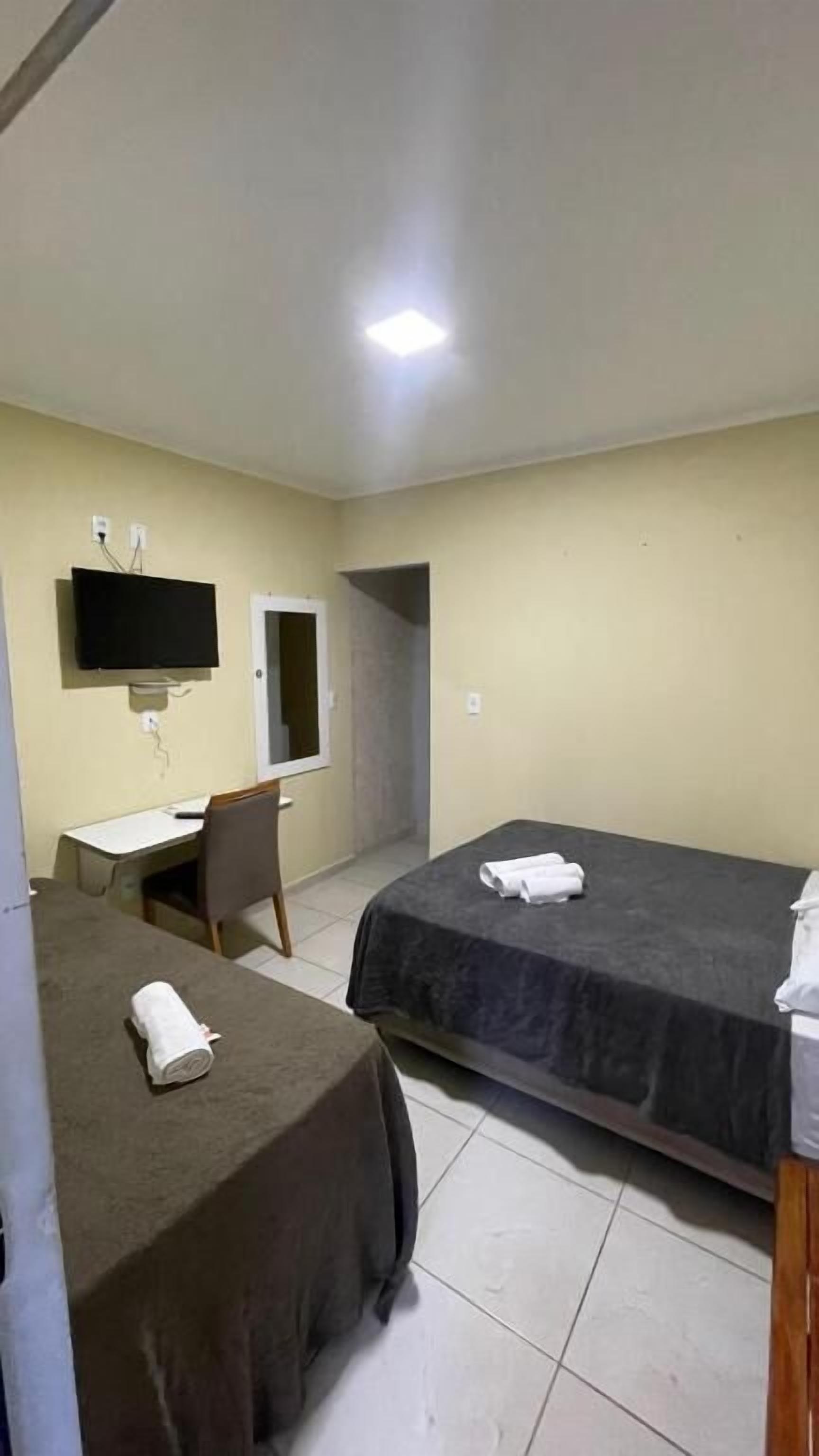 Quarto de hotel com duas camas, uma escrivaninha, uma cadeira, uma televisão e um espelho.