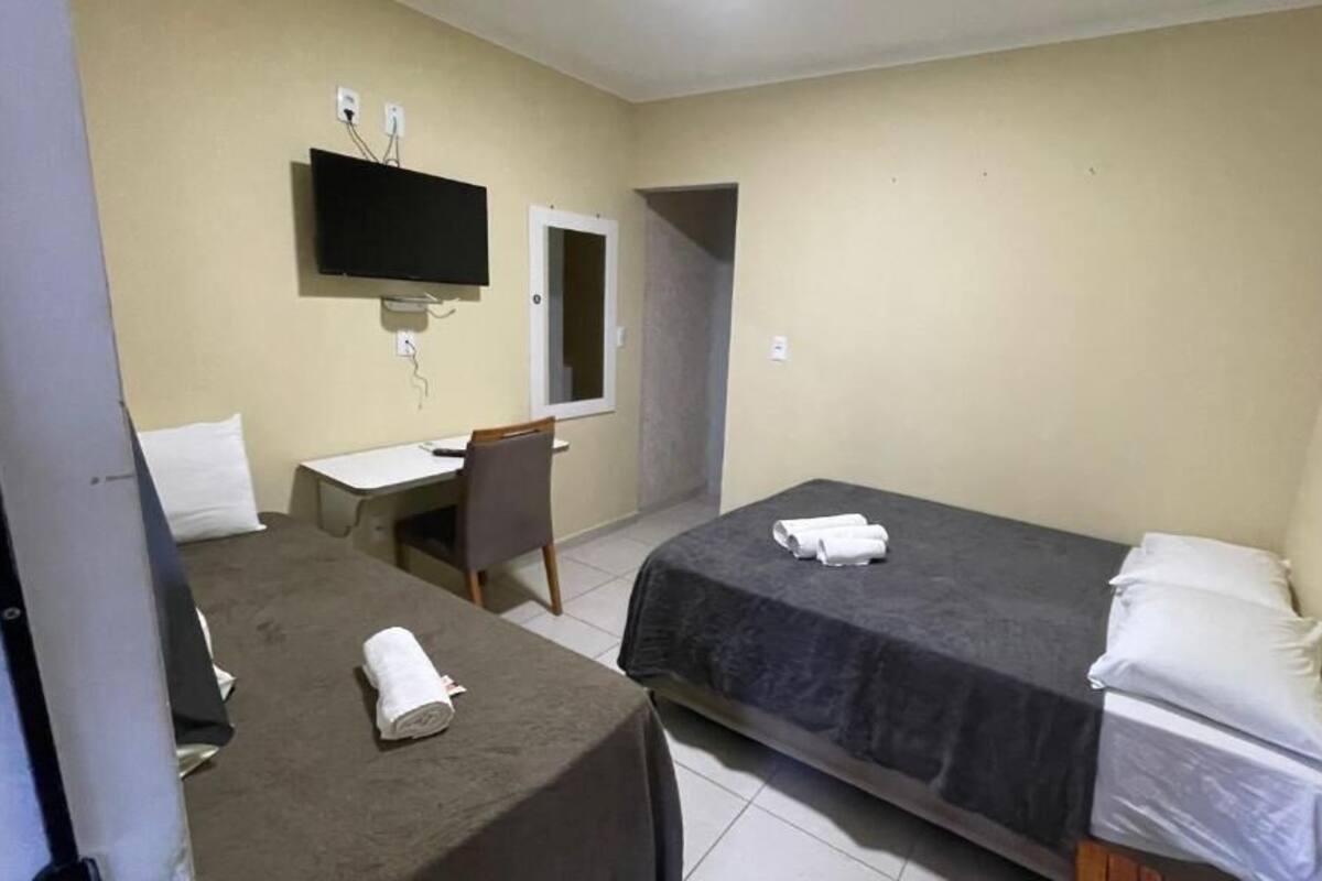Ein kleines Hotelzimmer mit Bett, Schreibtisch, Stuhl, Fernseher und Spiegel.