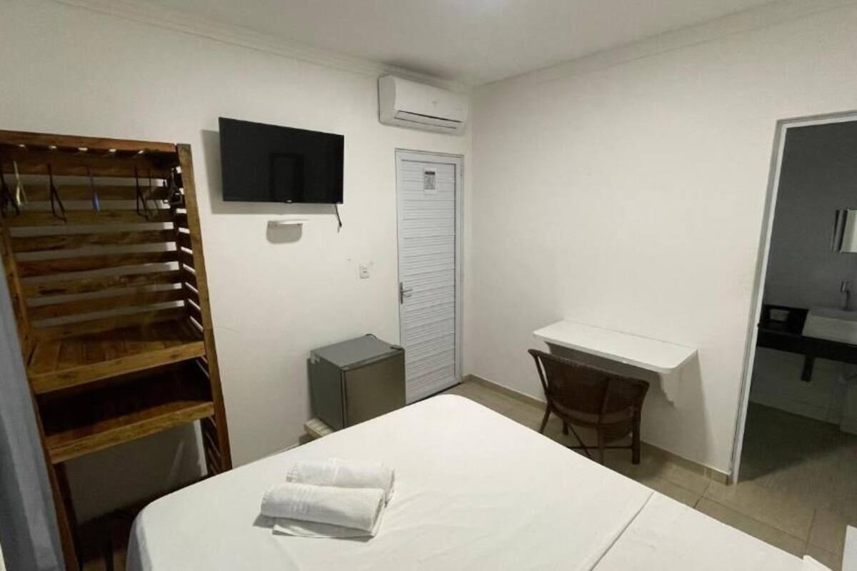 Ein Hotelzimmer mit Bett, Schreibtisch, Stuhl, Fernseher, Klimaanlage, Kleiderschrank und Bad mit Waschbecken und Spiegel.