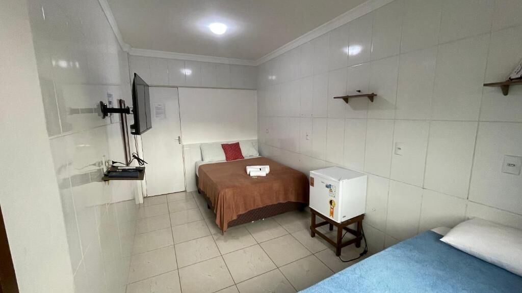 A hotel room with a bed, a small desk, a TV mounted on the wall, and a refrigerator.