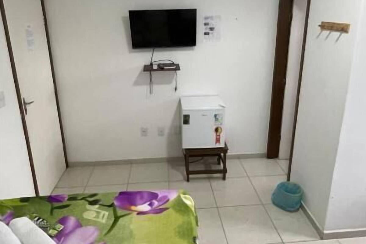 Ein Zimmer mit einem Bett, einem an der Wand montierten Fernseher, einem kleinen Tisch und einem Wasserspender.