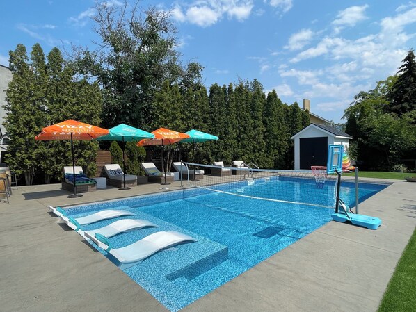 A swimming pool with lounge chairs and umbrellas, surrounded by trees. - 3BR Modern Kelowna Home w/ Pool & Sandy Beach Access (Kelowna)