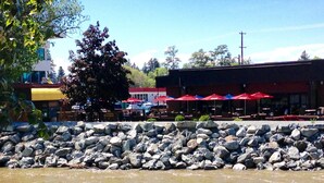 Un restaurant situé au bord de la rivière, doté d’une terrasse, d’une berge rocheuse et d’un bâtiment orné de parasols rouges.