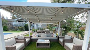 Une terrasse extérieure avec des meubles en osier, une table basse en verre et des guirlandes lumineuses.