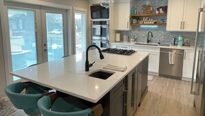 Une cuisine moderne dotée d’un îlot central, d’appareils électroménagers en acier inoxydable et de chaises de couleur turquoise.