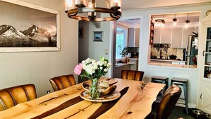 Un comedor con mesa de madera, sillas, una araña y un jarrón con flores.