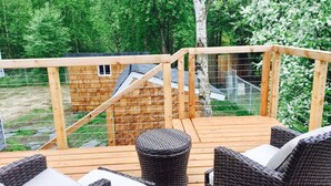 Una terraza de madera con muebles de mimbre y una pequeña construcción de madera al fondo.