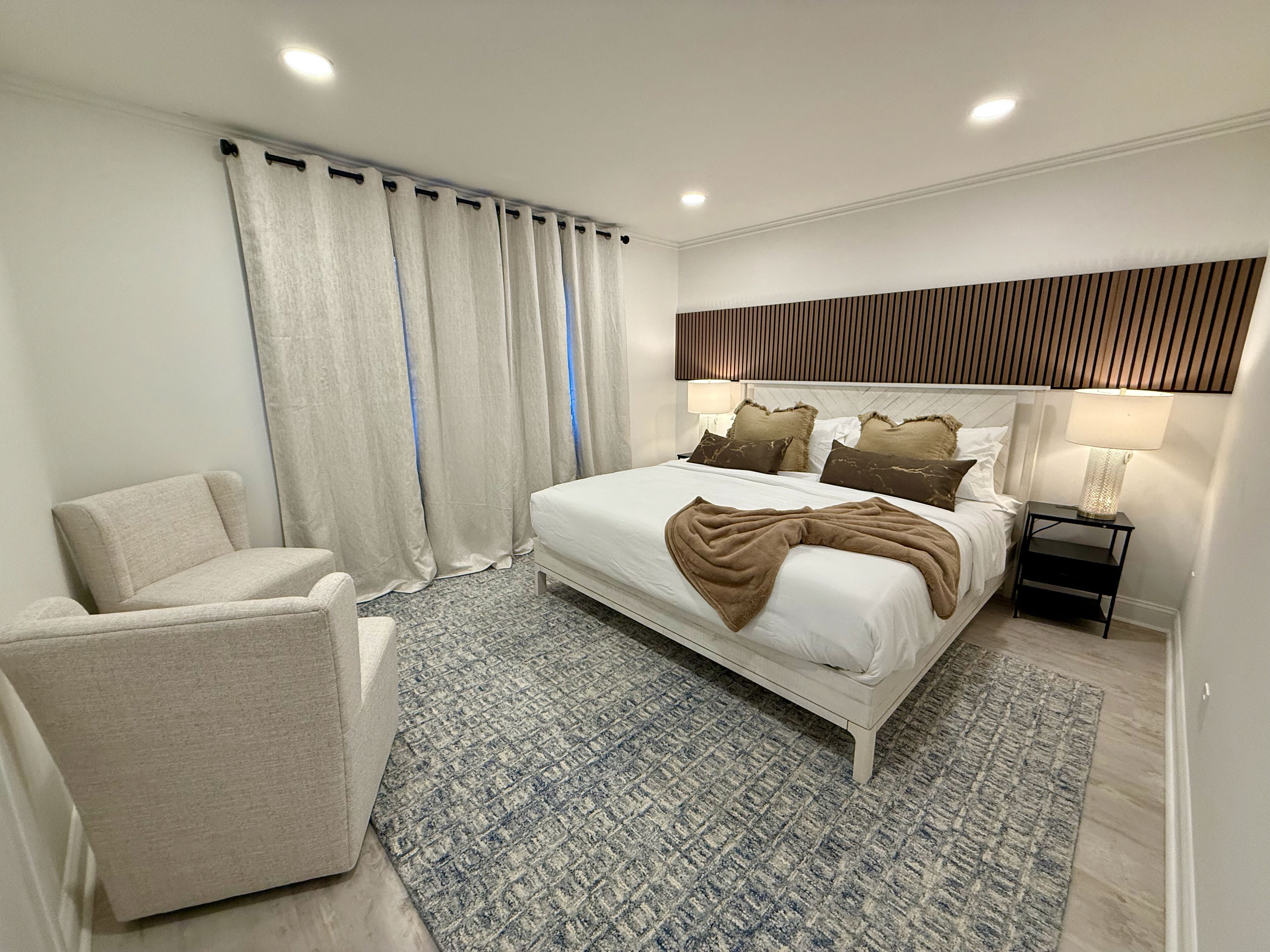 Une chambre à coucher moderne avec un grand lit, une chaise, une table de chevet et un tapis à motifs.
