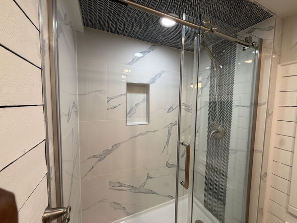A glass-enclosed shower with a herringbone-patterned ceiling and marble tiles.