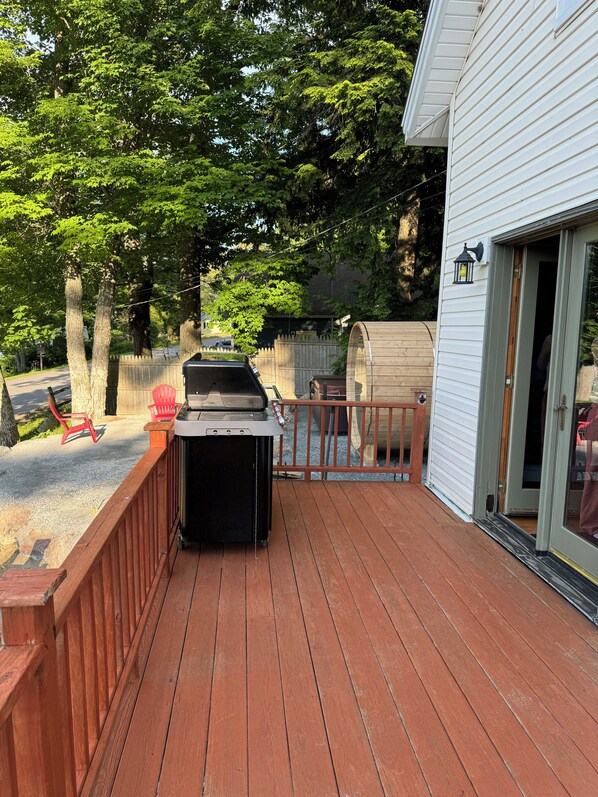 A wooden deck with a barbecue grill, a wooden fence, and a house with a sliding glass door. - New listing. Charming 3-bedroom lake house in Orrington WiFi, Hot tub, and Sauna (Orrington)