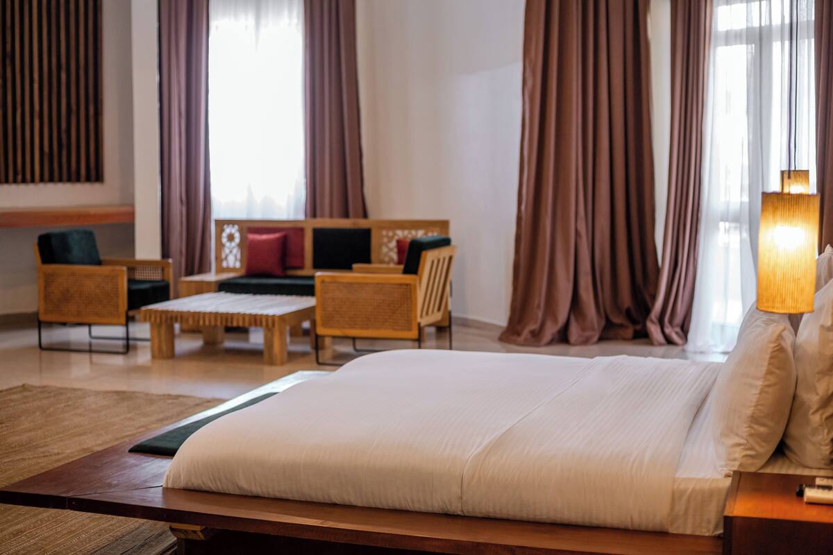 A hotel room with a large bed, a wooden nightstand, a desk, and two chairs.