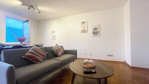 A modern living room with a grey sofa, a round coffee table, and a window with a view of a blue sky. - Charming vacation apartment in the heart of Koblenz's old town (Koblenz)