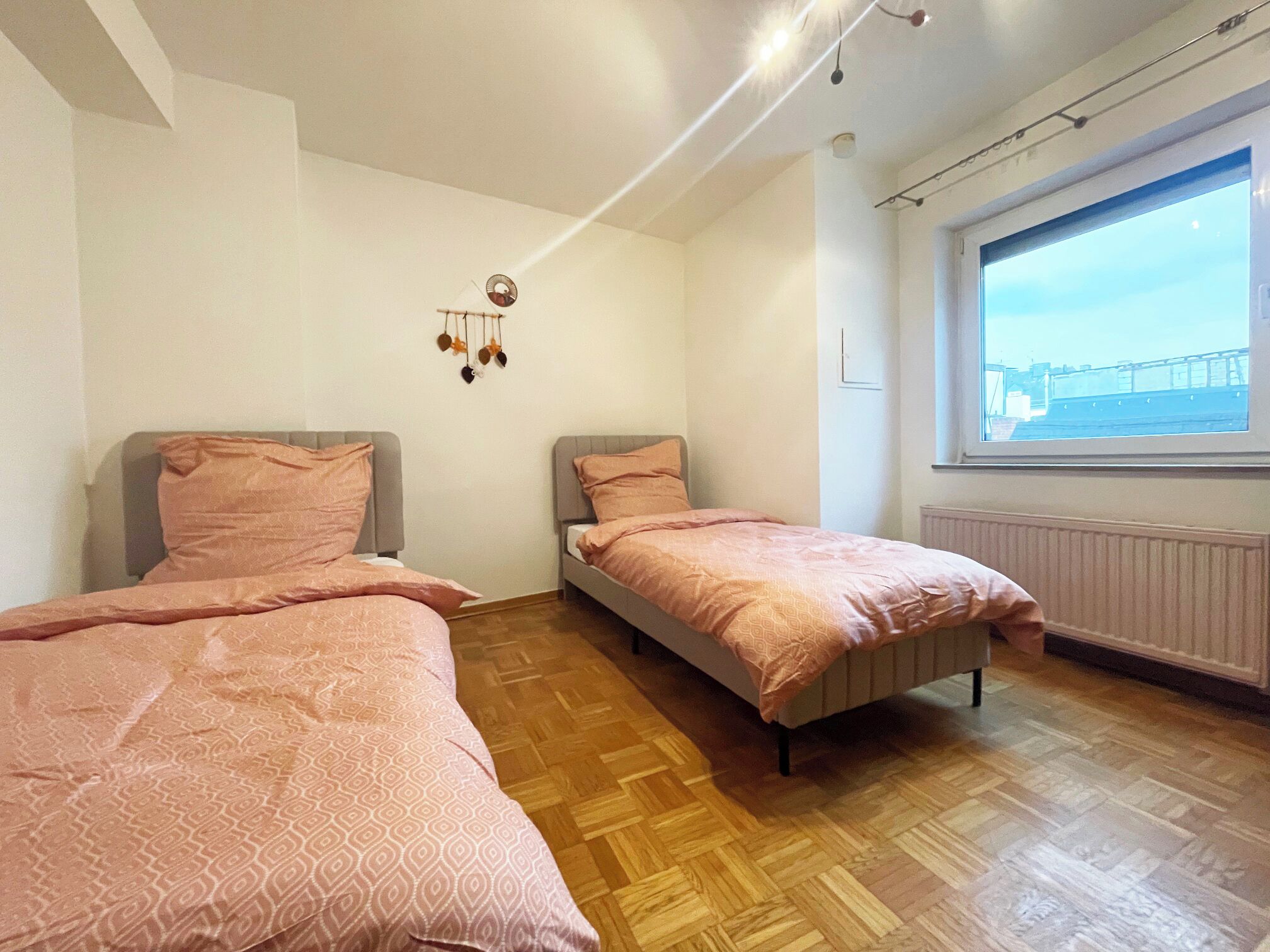 Una habitación con dos camas, piso de madera, una ventana con vistas y una lámpara colgante.