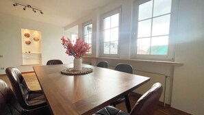 A dining area with a wooden table, black leather chairs, and a vase with red flowers. There are large windows providing natural light. - Charming vacation apartment in the heart of Koblenz's old town (Koblenz)