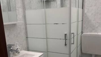 Een moderne badkamer met een douchecabine van glas, een wit wastafelmeubel en een toilet.