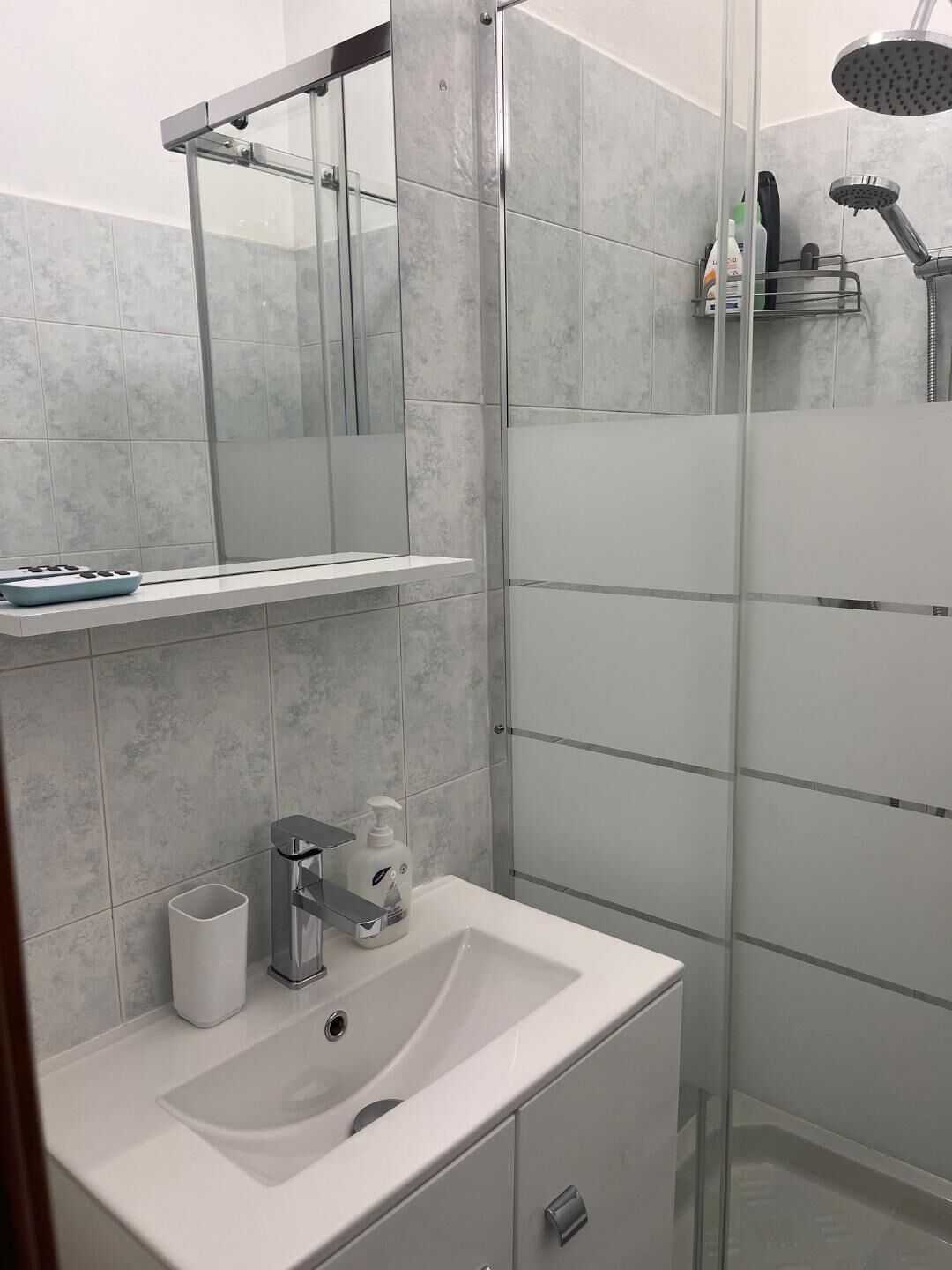 Ein modernes Badezimmer mit einer Duschkabine aus Glas, einem weißen Waschbecken und einem Spiegel darüber.