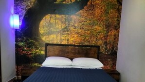 A bedroom with a bed, a nightstand, and a wall mural of a forest scene. - S.I.M residence (MANIAGO)