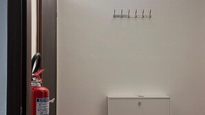 A hallway with a fire extinguisher mounted on the wall, a white filing cabinet, and a wall-mounted light fixture. - S.I.M residence (MANIAGO)
