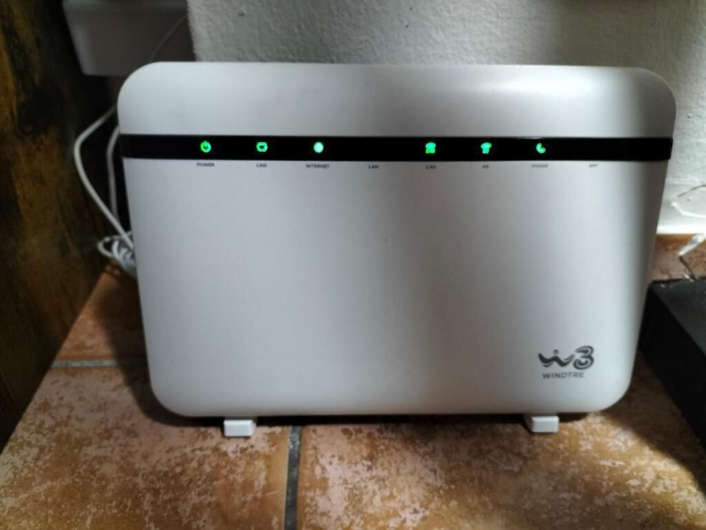Un appareil rectangulaire blanc, orné d’une bande noire et de voyants verts indiquant « ALIMENTATION », « RÉSEAU LOCAL », « INTERNET » et « RÉSEAU LOCAL », le tout placé sur une surface carrelée.
