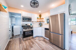 A compact kitchen with white cabinets, stainless steel appliances, and a wooden floor.