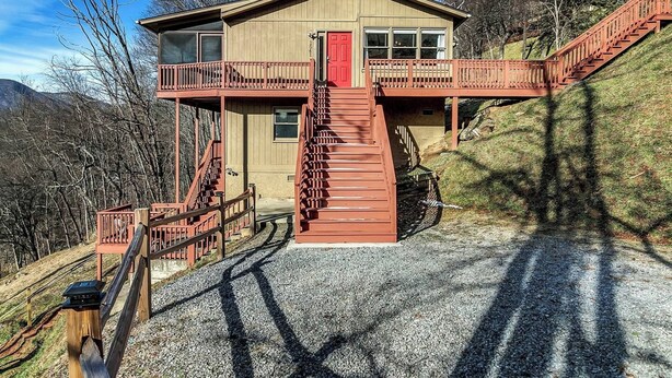 A two-story cabin with a red door and a balcony, surrounded by trees and hills. - Cragmont Rentals (Black Mountain)