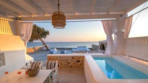 Zona de piscina con vista al mar, paredes de piedra y una mesa con sillas y un bol.