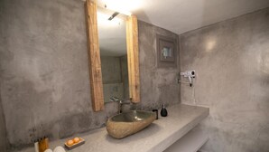 Un baño con un lavamanos grande y ovalado de piedra, un espejo con marco de madera y un toallero empotrado con toallas y artículos de aseo.