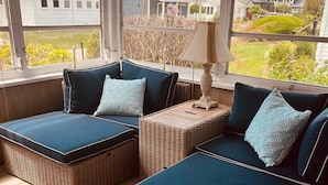 A cozy room with wicker furniture and a view of houses through large windows. - Charming Beach Cottage, Steps to Beach, Enjoy Scenic Vineyards & Farm Stands (South Jamesport)