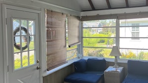 A covered porch with a ceiling fan, wicker furniture, and a view of the outdoors. - Charming Beach Cottage, Steps to Beach, Enjoy Scenic Vineyards & Farm Stands (South Jamesport)