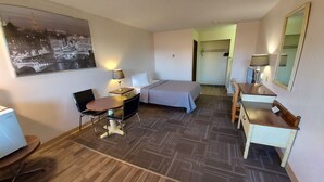 A hotel room with a bed, a desk with a lamp, a chair, a small table, and a mirror. - HOO - DOO MOTEL (Drumheller)