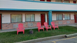 A motel with numbered rooms, red doors, and a row of red chairs outside. - HOO - DOO MOTEL (Drumheller)