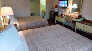A hotel room with two beds, a desk with a computer and a television, a mirror, and a lamp. - HOO - DOO MOTEL (Drumheller)