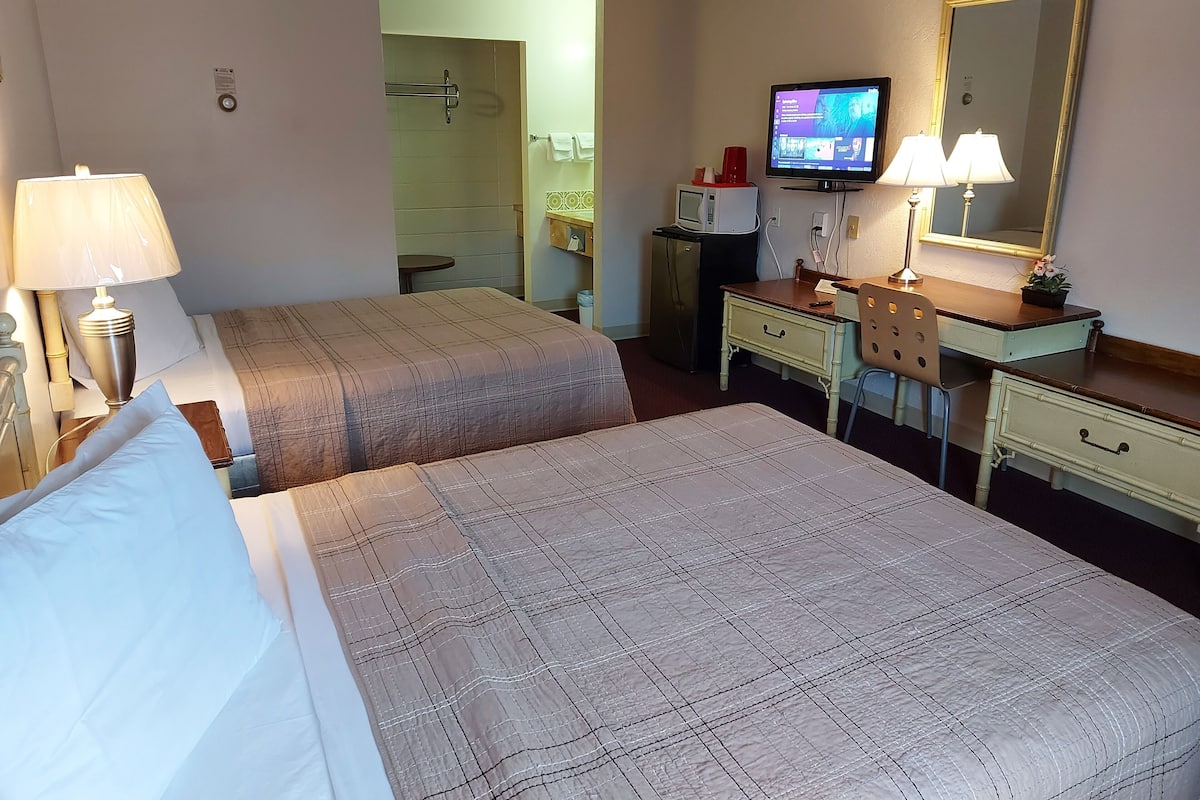 A hotel room with two beds, a desk with a computer and a television, a mirror, and a lamp.