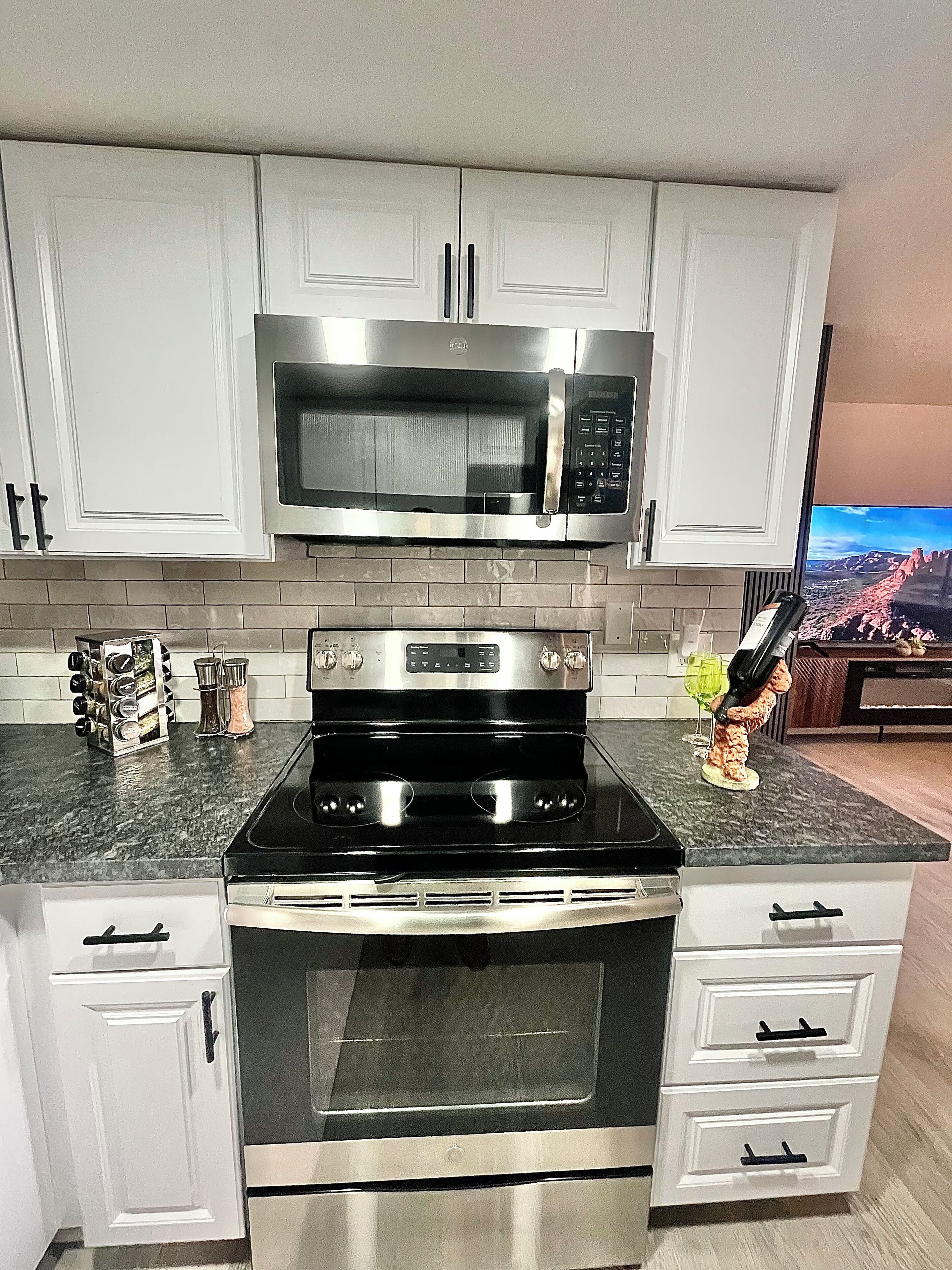 A kitchen with white cabinets, a stainless steel microwave, a black stove, and a wine bottle on the counter.