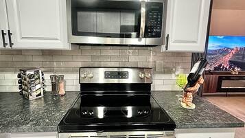 A kitchen with white cabinets, a stainless steel microwave, a black stove, and a wine bottle on the counter.
