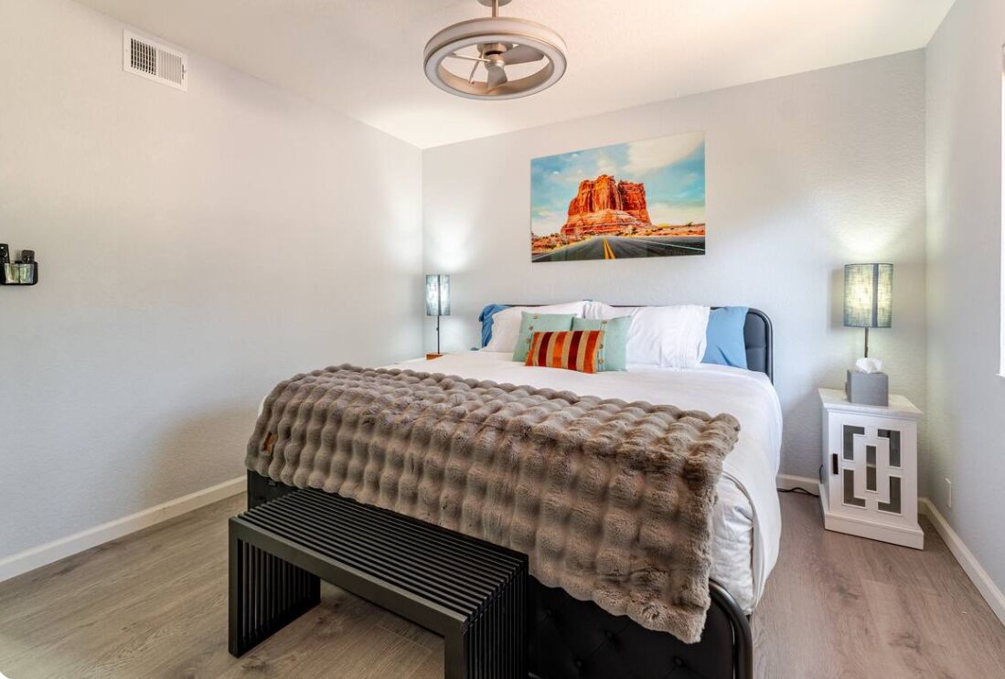 Une chambre à coucher comprenant un lit, un banc, une table de chevet, une lampe et un tableau accroché au mur.