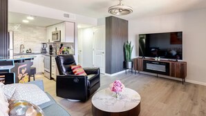 A modern living room with a black leather sofa, a round coffee table with a vase of flowers, a flat-screen TV, and a kitchen in the background. - Charming Red Rock Poolside Condo with WiFi, AC in superb Sedona (Sedona)