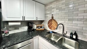 A kitchen with white cabinets, a granite countertop, a double sink, a coffee maker, and a wooden cutting board hanging on the wall. - Charming Red Rock Poolside Condo with WiFi, AC in superb Sedona (Sedona)
