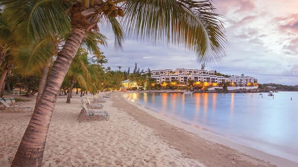 A beachfront hotel with a row of beach chairs, a sandy beach, and a calm sea with boats. - Studio Double @ WorldMark Elysian Beach Resort (St Thomas)