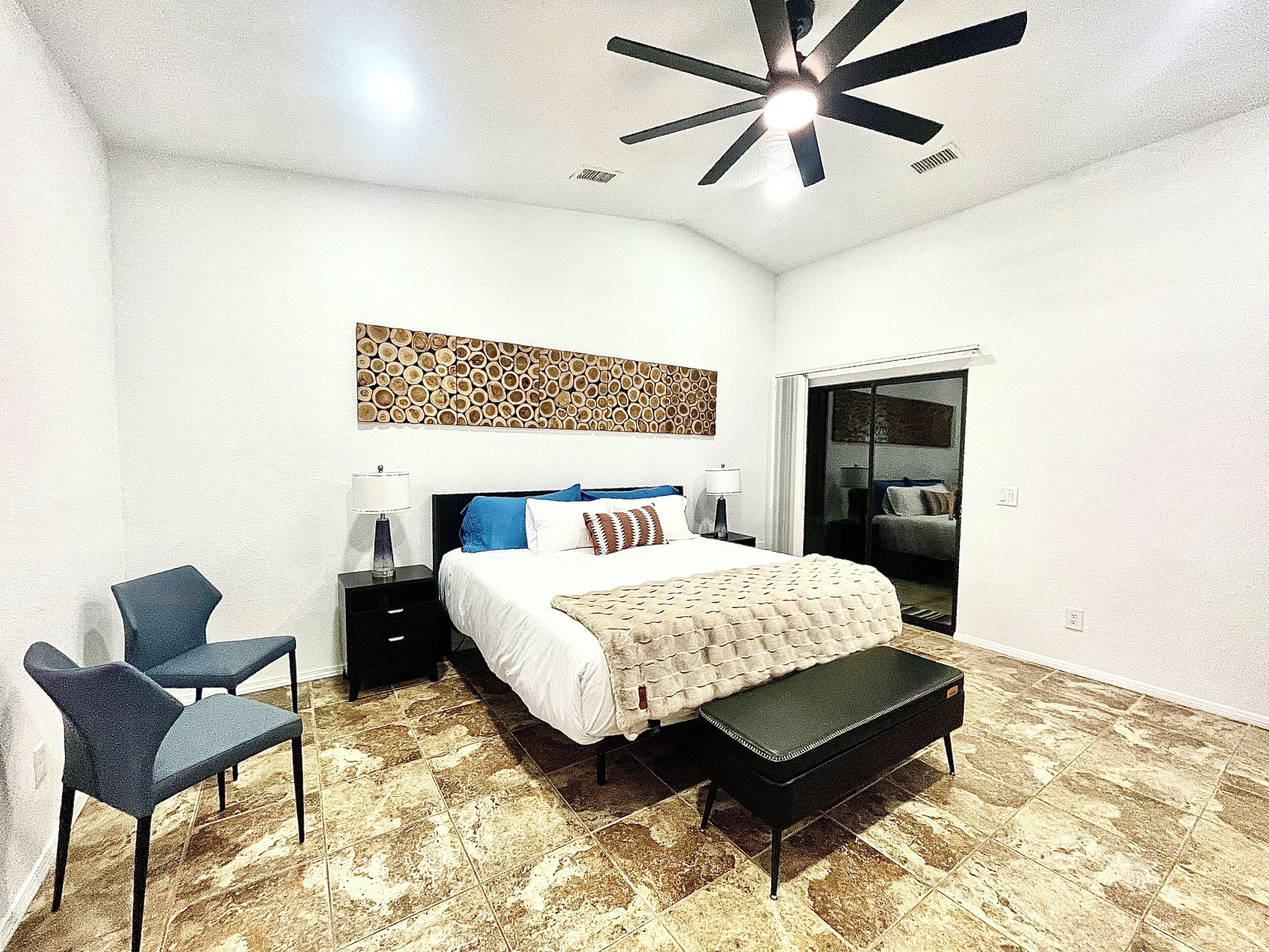 A bedroom with a bed, a bench, a chair, a ceiling fan, and a patterned wall.