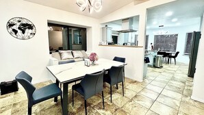 Een eetgedeelte met een witte tafel, vier stoelen, een wereldbol als wanddecoratie en een moderne kroonluchter.