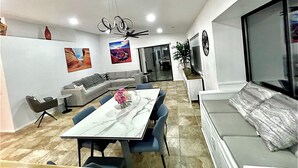 Een moderne woonkamer met een eetgedeelte, een grijze bank, een televisie en een plafondventilator.