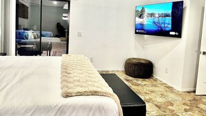 Een moderne hotelkamer met een groot bed, een bankje, een televisie aan de muur en een schuifdeur naar een balkon.