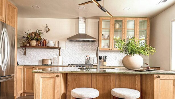A modern kitchen with wooden cabinets, a stainless steel refrigerator, a large island with stools, and a backsplash with a geometric pattern. - Spacious 3BR Home - Fast Wifi - Parking - BBQ - Patio - Garden (Williston)