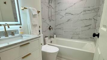 A modern bathroom with a marble shower wall, a freestanding bathtub, and a vanity with gold handles.