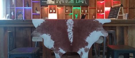 A rustic bar with a sign reading "RANCH BAR" and a cowhide table in the foreground.